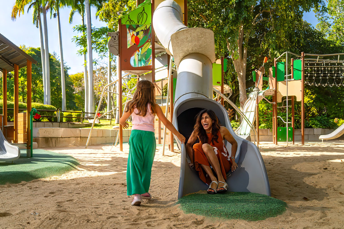 A woman sliding down a slide with a young girl offering help to get out of the slide