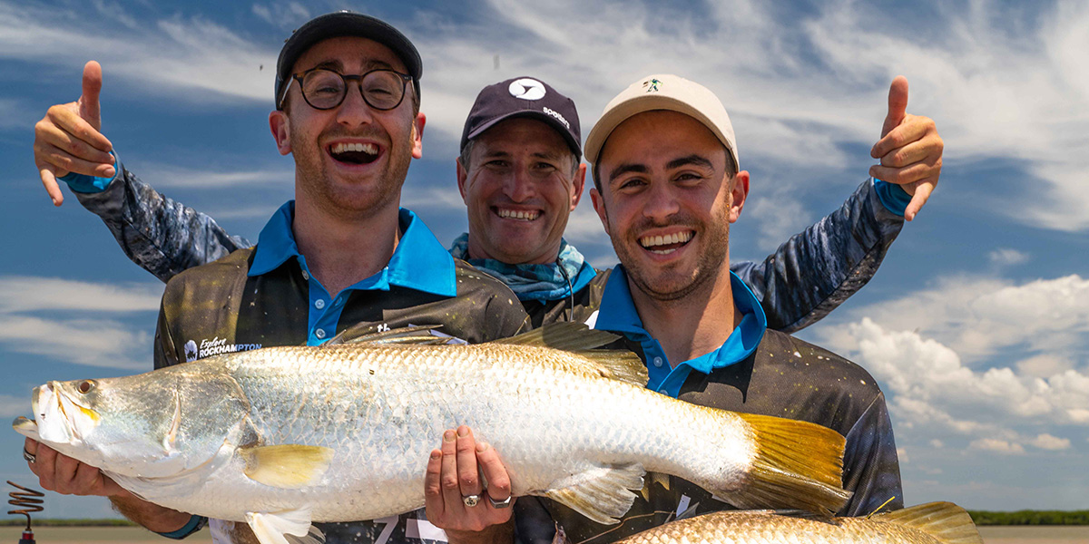 Three men on a boat holding a barramundi