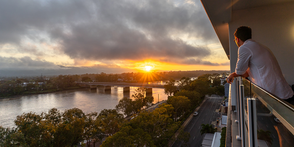 a man taking in a sunset river view from the balcony of the hotel