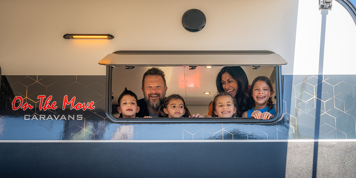 Family of six staring out the window of a caravan smiling at the camera.