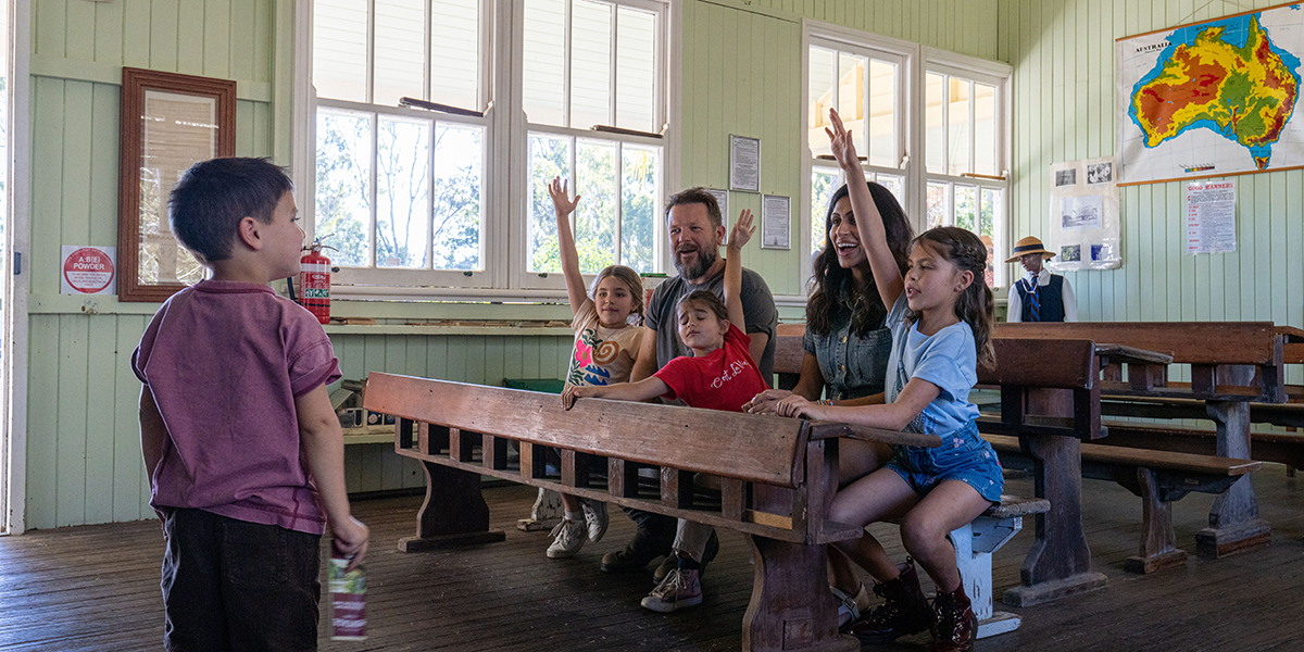 Family of six sitting in a historical school classroom at the Rockhampton Heritage Village.