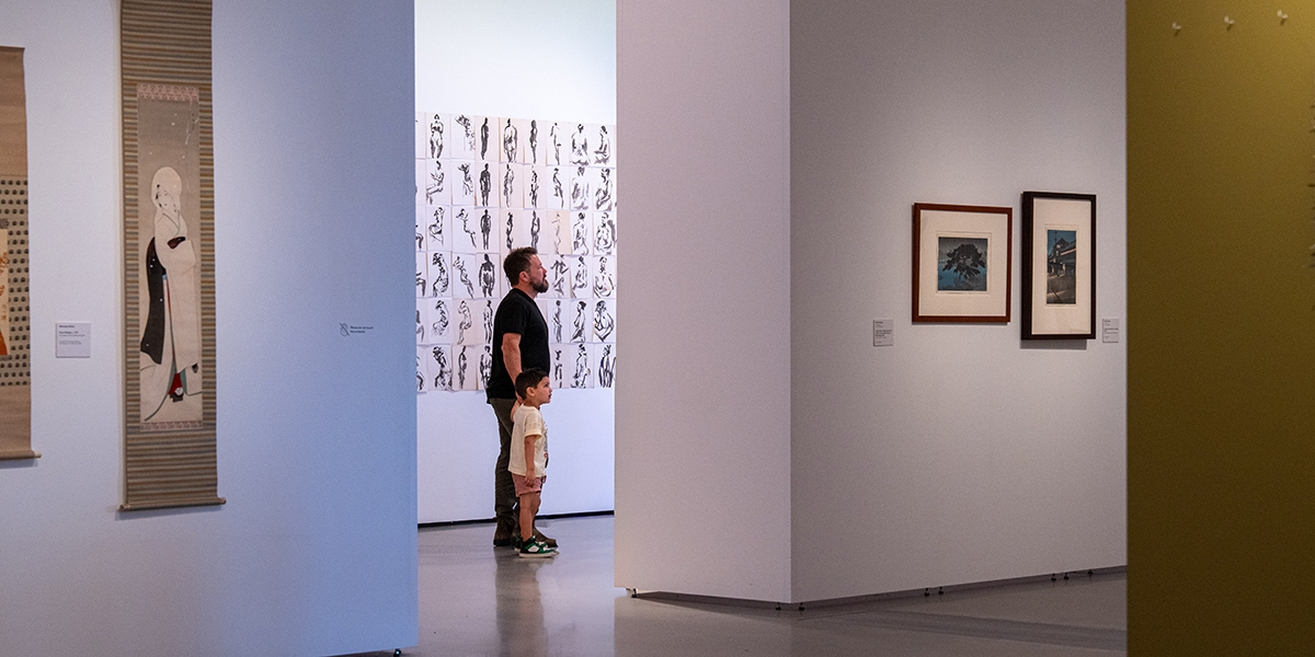 Father and son looking at artwork hung on a wall between a walkway.