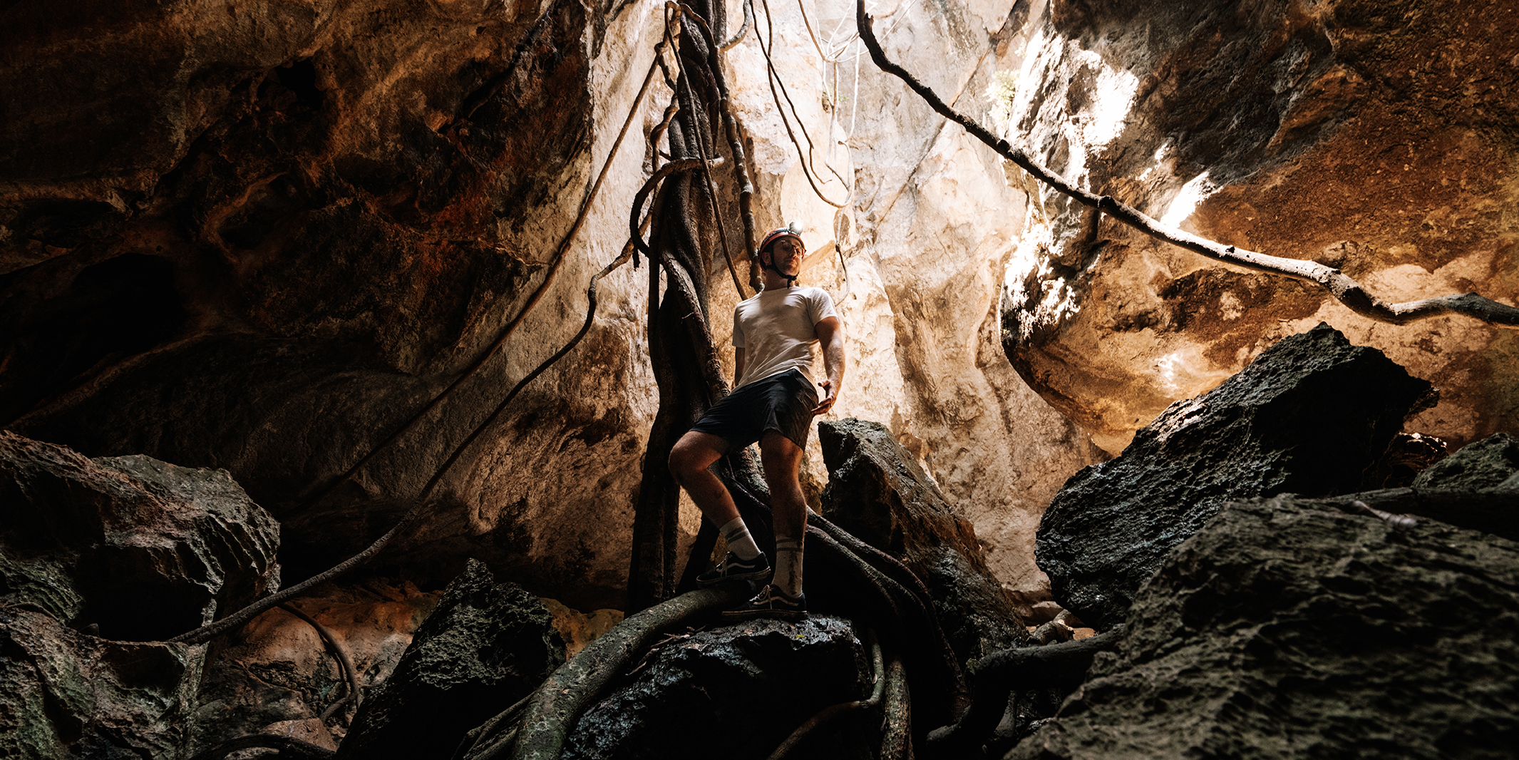 Man standing on giant rocks looking up through the cave ceiling