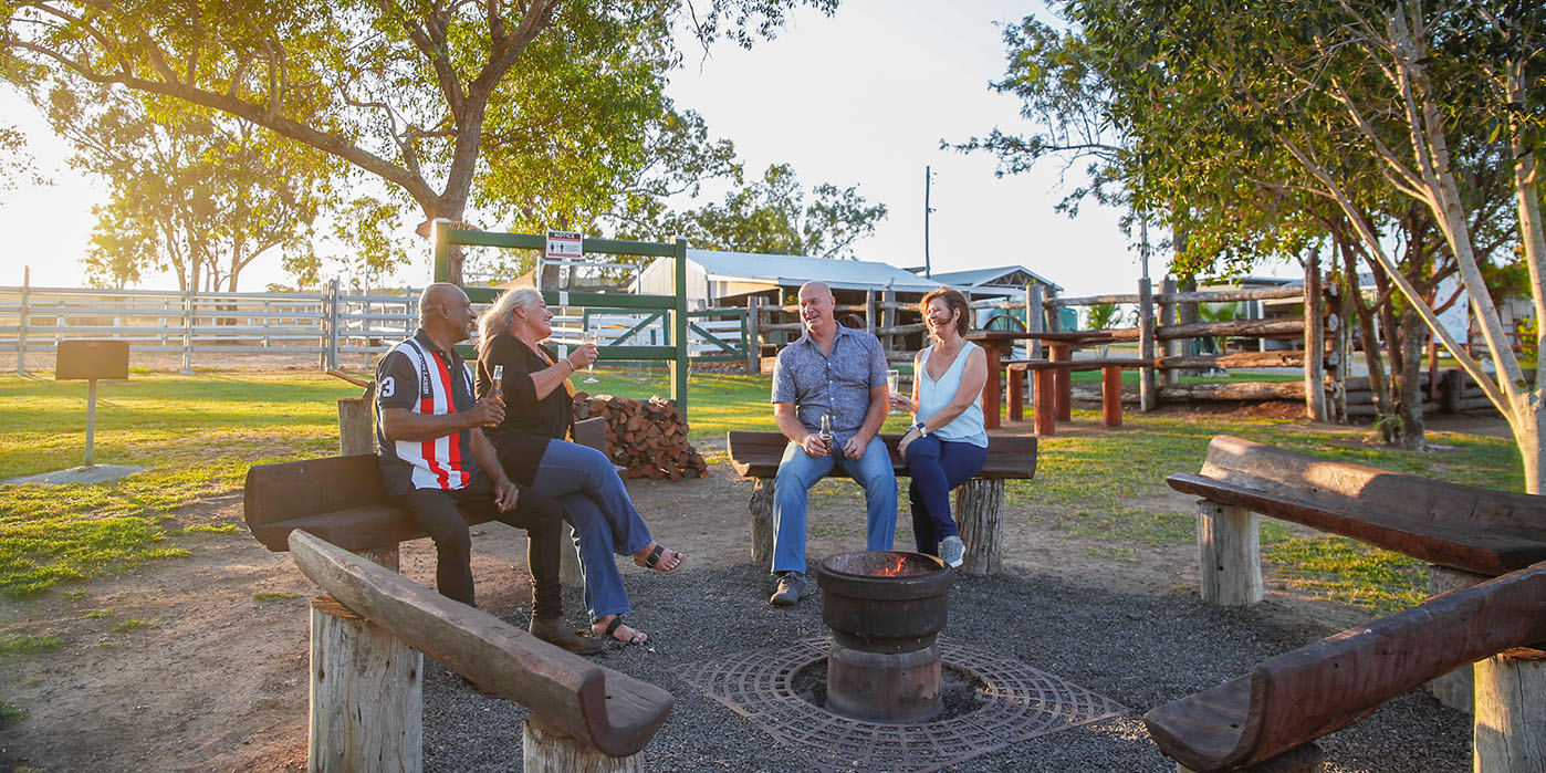 Two older couples sharing stories by a fire pit at a local farm stay.