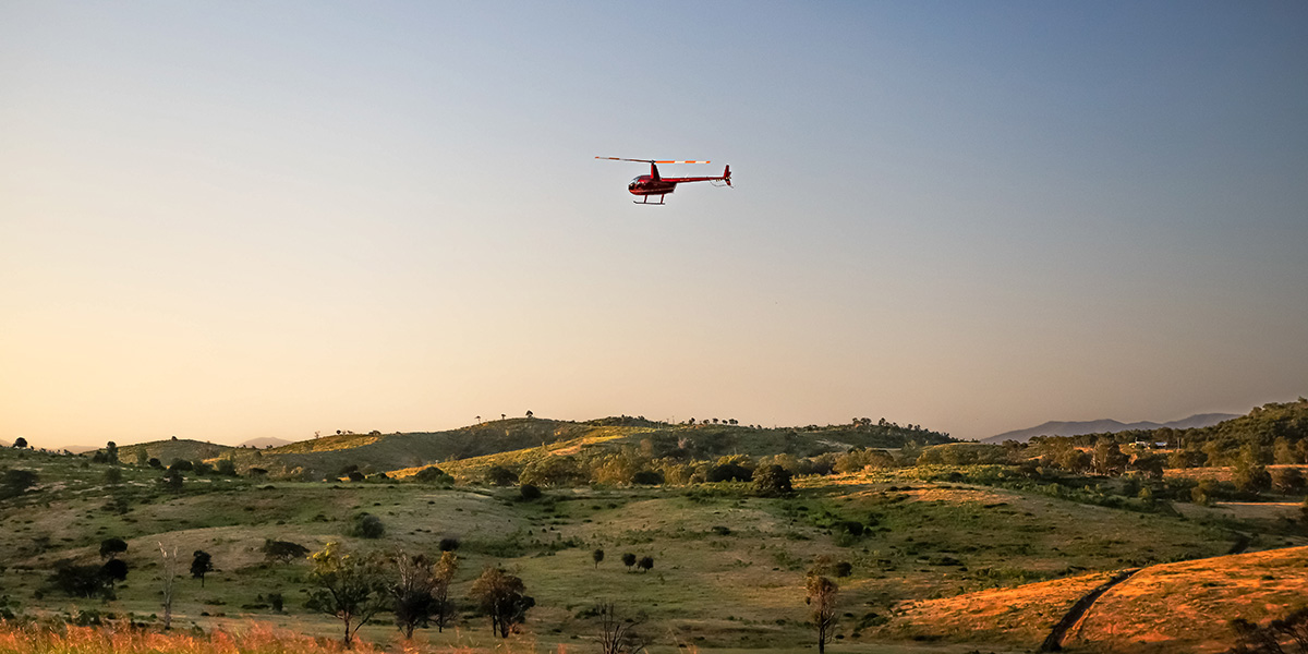 Red helicopter flying over fast plains upon dusk