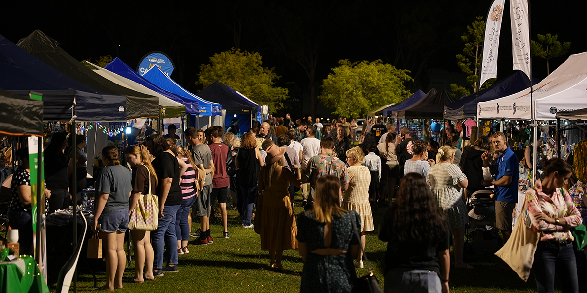 Crowd surrounds market stalls at the Rockhampton Heritage Village in the evening