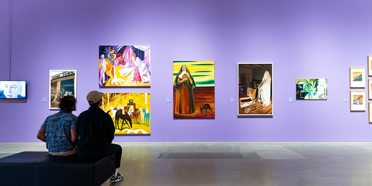 Two men sitting down looking at artowrk in a gallery.
