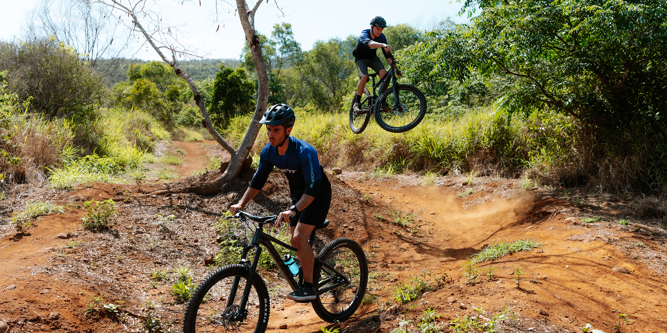 Two young men ride the Mount Archer First Turkey Mountain Bike Trails smiling.