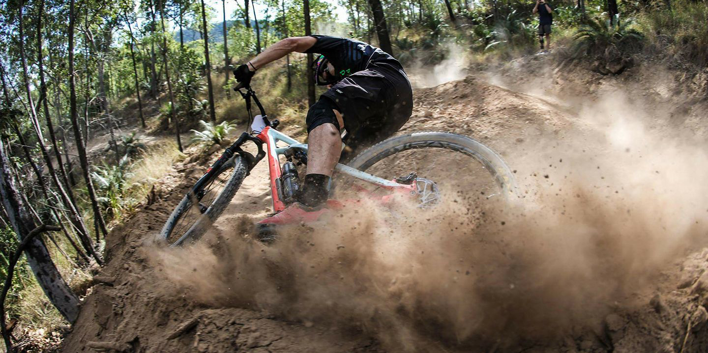 Mountain bike rider taking a corner on a dirt trail flicking up dust and debris.