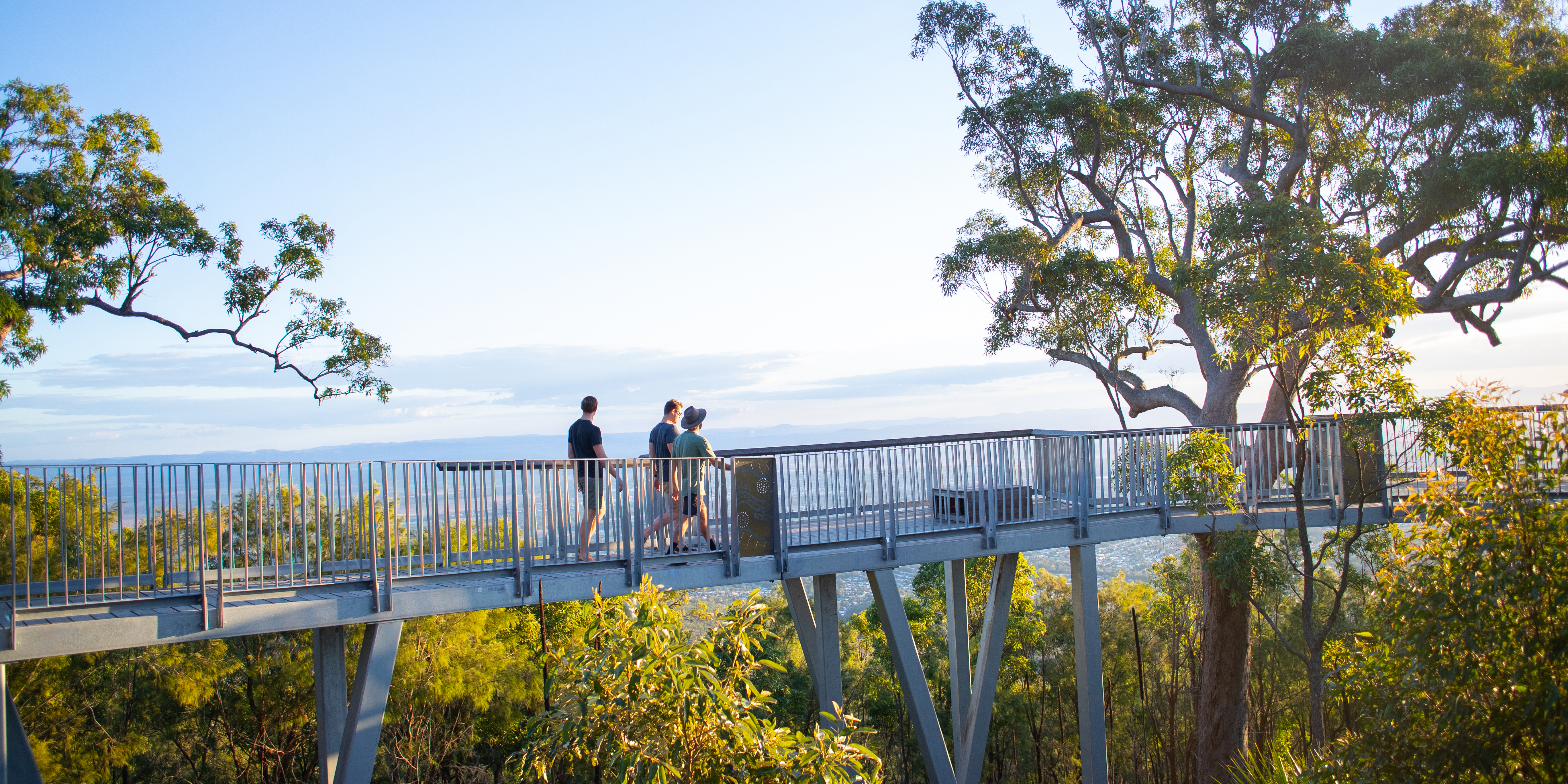 Three hikers walking along an elevated boardwalk overlooking mountains