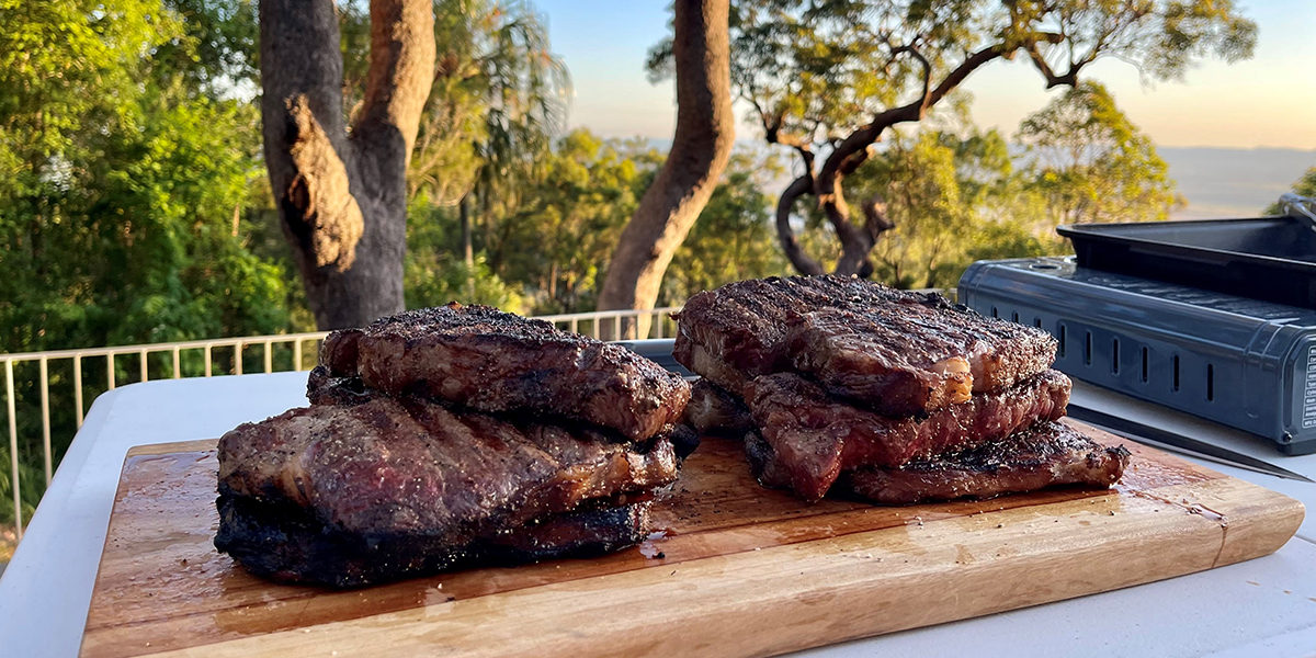 Mouth-watering steak stacked on a cutting board with a beautiful bush land view in the background.