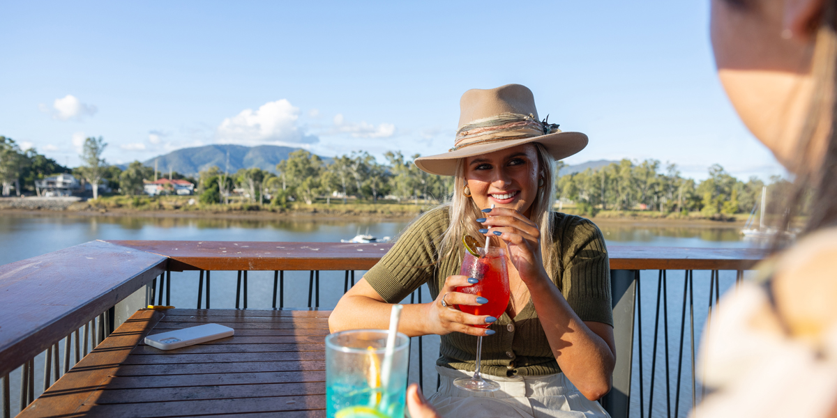 Young woman smiling with a cocktail in her hand with a river view in the background