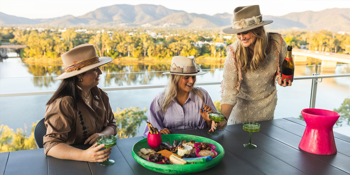 Three women enjoying cheese and champagne on their hotel balcony overlooking the river and mountains.