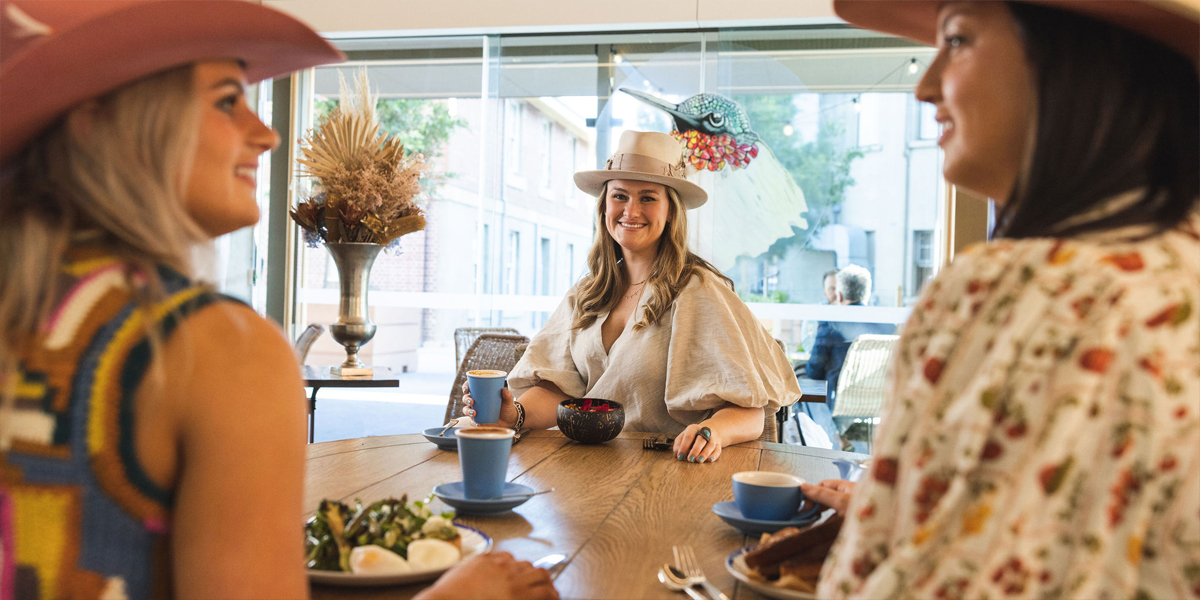 3 women sitting around a table enjoying breakfast and smiling.