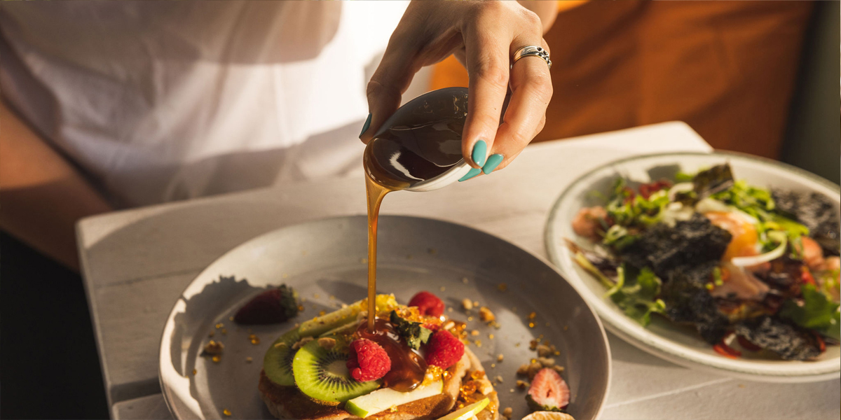 Close up of a hand pouring syrup over fruit and toast breakfast dish