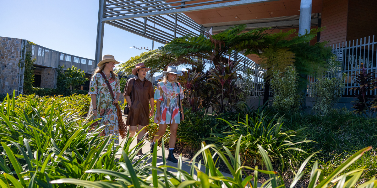 Three young women walking along a footpath outside a major shopping centre.