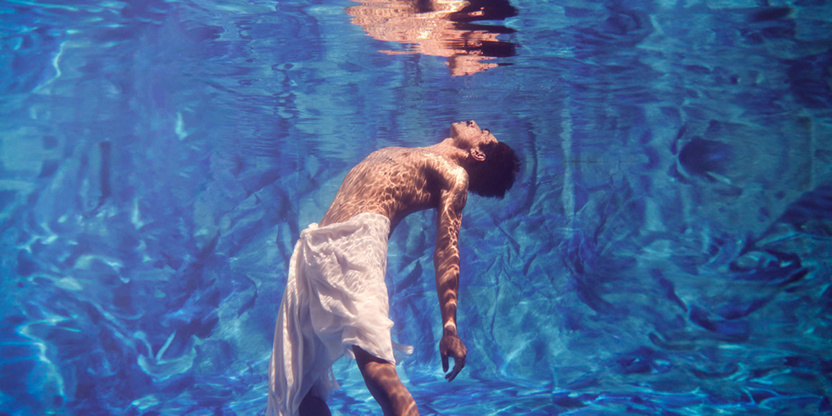 Male dancer under water arching his back with his face about to break the surface of the water.