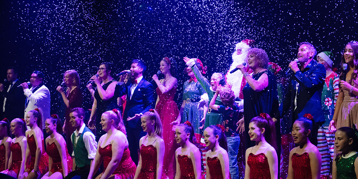 people singing on stage whilst fake snow falls from the sky