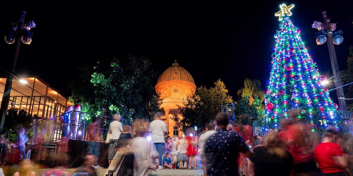 People enjoying the night time activities in front of a giant lit Christmas Tree