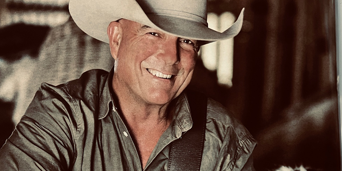 Headshot of country music singer James Blundell holding a guitar smiling.