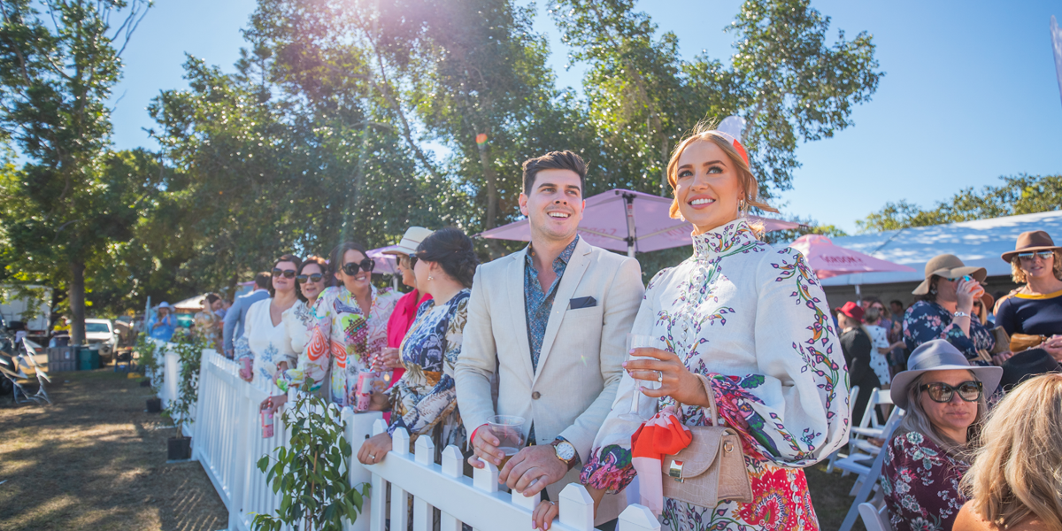 well dressed couple standing at picket fence holding champagne