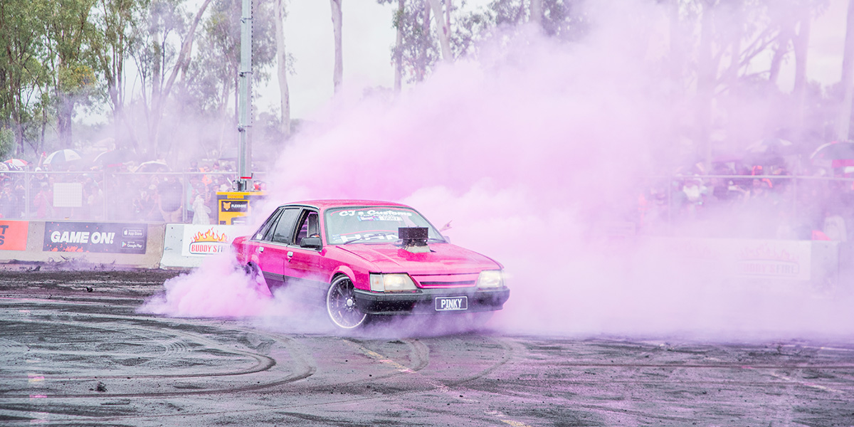 A red car does a burnout with pink smoke at the Rockhampton riverfront