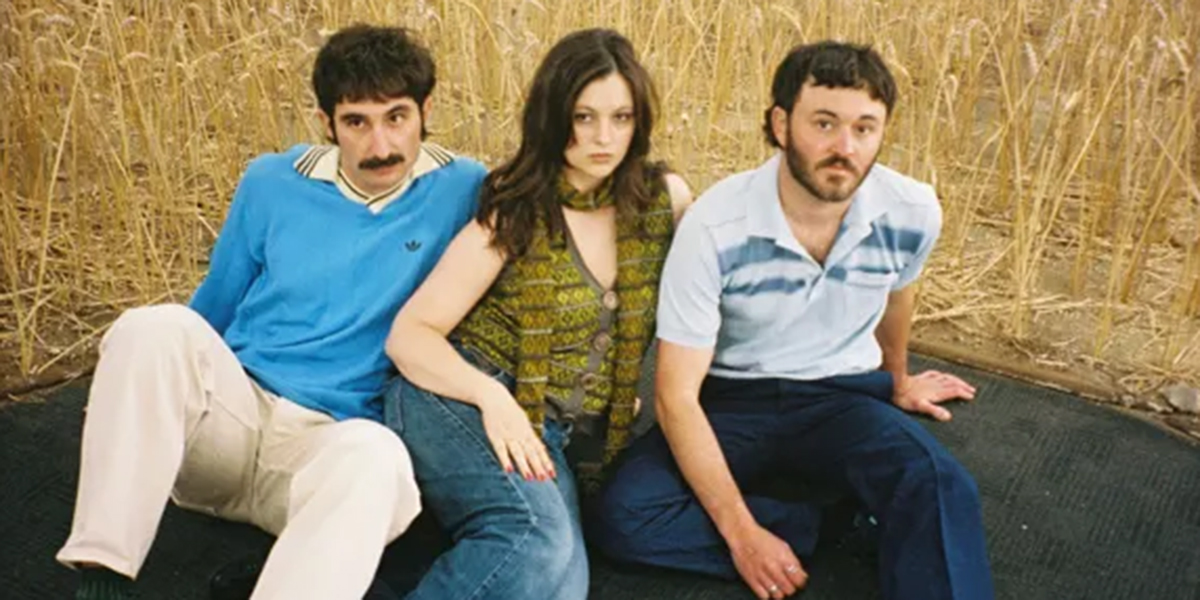 Two guys and a young women sitting on the ground wearing vintage clothing