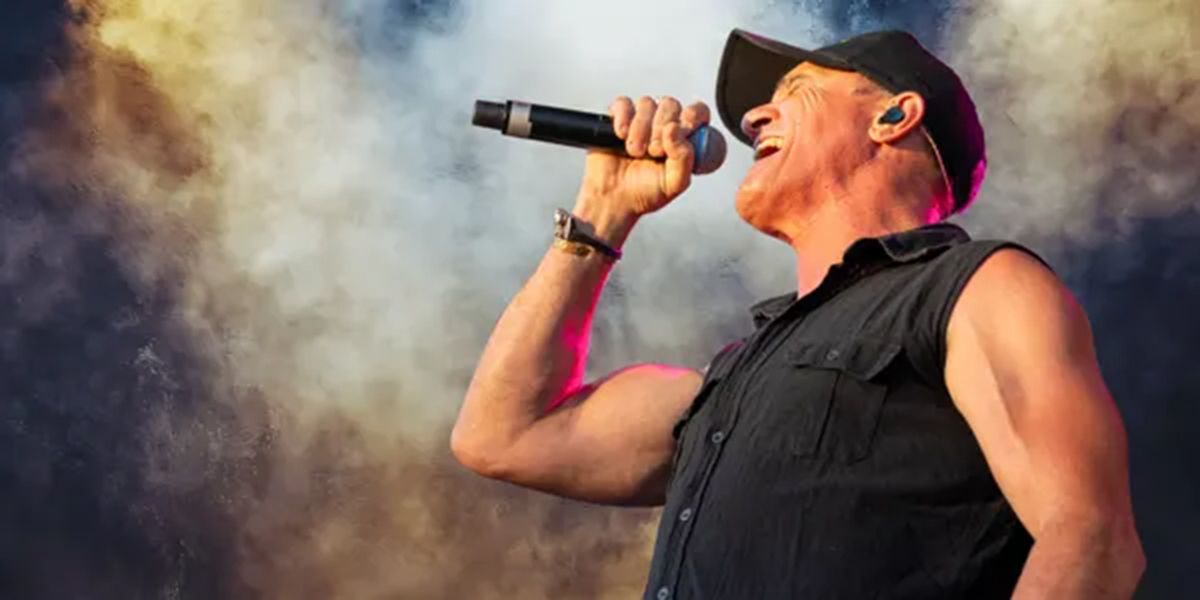 Side profile of Shannon Noll singing into a microphone with a smoky background.