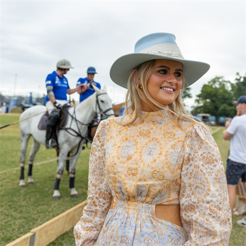 well dressed lady standing in front of polo players on horses