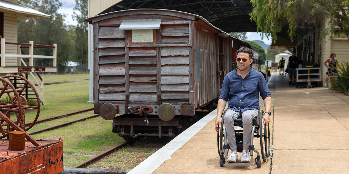 A man in a wheelchair exploring a vintage train platform with a vintage train in the background