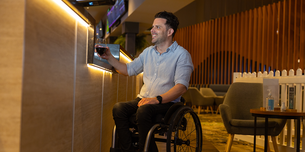 A man in a wheelchair purchasing a drink from a lowered bar counter