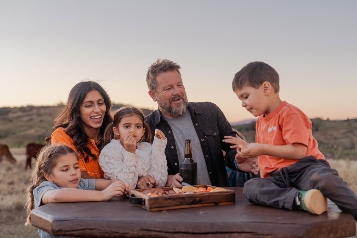 Family sharing food at a wooden table on a farm