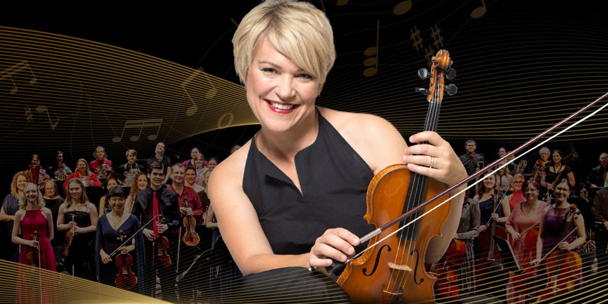 a woman with short blonde hair holding a violin with an orchestra in the background.