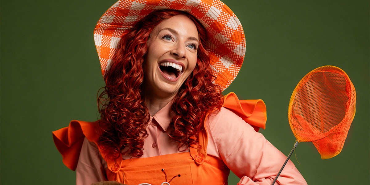 Young woman wearing vibrant orange coloured clothes, smiling and holding a butterfly net.